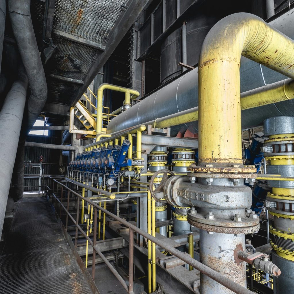 Close-up of an intricate industrial pipeline system featuring yellow valves and steel structures inside a factory.